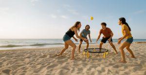 Cuatro jóvenes jugando a Spikeball en la playa al atardecer